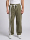 Men’s black wide-leg track pants with olive-green side stripes, styled with a white T-shirt and white sneakers.