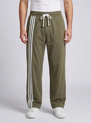Men’s black wide-leg track pants with olive-green side stripes, styled with a white T-shirt and white sneakers.