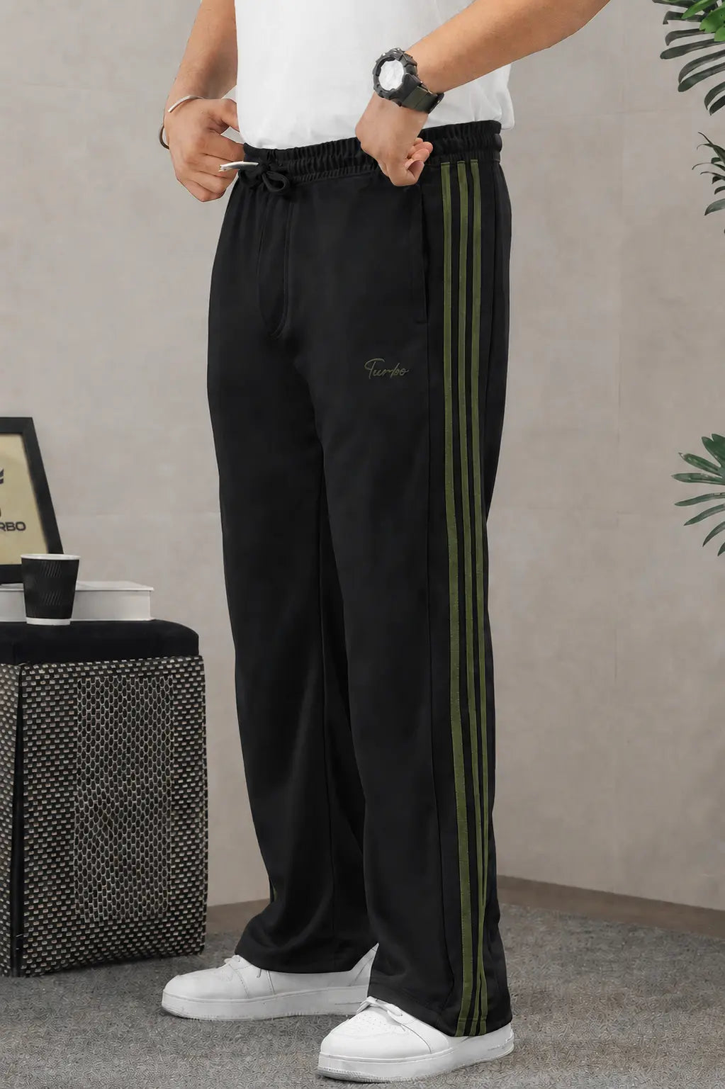 Men’s black wide-leg track pants with olive-green side stripes, styled with a white T-shirt and white sneakers.